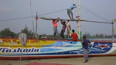 Toma-En-Cámara-Lenta-De-Marineros-Trabajando-En-Equipo-En-Un-Barco-Colorido-En-La-Playa-De-Arena-De-La-Jungla,-Weligama,-Sri-Lanka