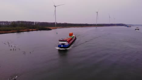 Luftaufnahme-Des-Martie-frachtschiffs,-Das-Auf-Der-Oude-Maas-Vorbeifährt,-Mit-Wegfliegenden-Vögeln-Und-Stillstehenden-Windturbinen-Im-Hintergrund