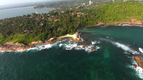 FPV-video,-view-from-above,-aerial-view-from-an-FPV-drone-flying-at-high-speed-over-a-green-coast-with-a-beautiful-white-sand-beach-bathed-by-a-turquoise-water