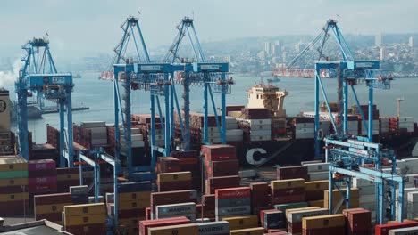 Contenedores-Apilados-Cerca-De-Grúas-Esperando-Ser-Cargados-En-Un-Buque-De-Carga-Atracado-En-El-Puerto-Marítimo-De-Valparaíso,-Chile