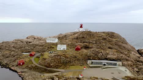 Downward-moving-aerial-with-tilt-up-of-Lindesnes-lighthouse-and-museum-with-visitors-and-tourists-walking-around-on-location---Atlantic-ocean-and-horizon-in-background