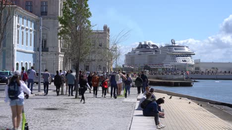 Gente-Caminando-Por-El-Paseo-Marítimo-A-Lo-Largo-Del-Río-Tajo,-Crucero-Amarrado-En-El-Puerto-De-Cruceros-De-Lisboa