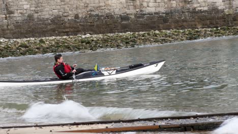 Male-in-safety-life-jacket-rowing-kayak-on-Welsh-seaside-waves