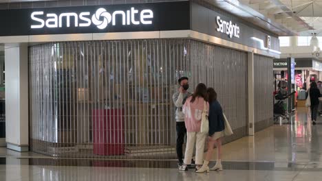 Passagiere-Gehen-An-Einem-Geschlossenen-Amerikanischen-Gepäckhersteller-Und--händler-Vorbei,-Einem-Samsonite-geschäft-Am-Internationalen-Flughafen-Hongkong,-Da-Die-Meisten-Unternehmen-Aufgrund-Der-Ausbreitung-Der-Covid-19-variante-Geschlossen-Sind