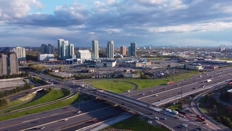 Highway-401-with-trucks,-cars,-Go-Transit-bus-driving-by-Scarborough-Town-Centre-with-large-shopping-mall,-big-box-stores-and-condo-developments