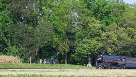 Una-Vista-De-Un-Tren-De-Pasajeros-De-Vapor-Antiguo,-Viajando-A-Través-De-Tierras-De-Cultivo,-Deteniéndose-En-Una-Pequeña-área-De-Picnic,-Soplando-Humo-Y-Vapor-En-Un-Día-De-Otoño-Temprano