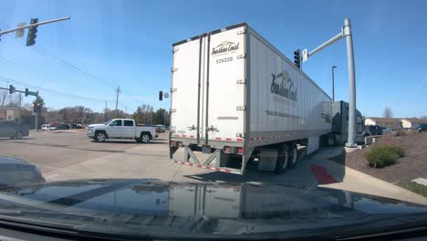 POV-while-following-a-semi-truck-and-trailer-around-a-corner-at-a-stop-light-with-traffic