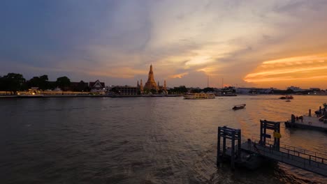 Farbenfroher-Sonnenuntergang-Im-Zeitraffer-Am-Chao-Phraya-Flussufer-Mit-Kreuzfahrtbooten,-Die-Am-Wat-Arun-Tempel-Vorbeifahren