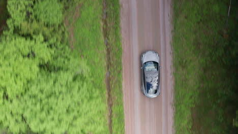 Luftaufnahme-Von-Oben-Nach-Unten---Ein-Tesla-Model-3-Fährt-Eine-Unbefestigte-Straße-In-Einem-Wald-Hinunter