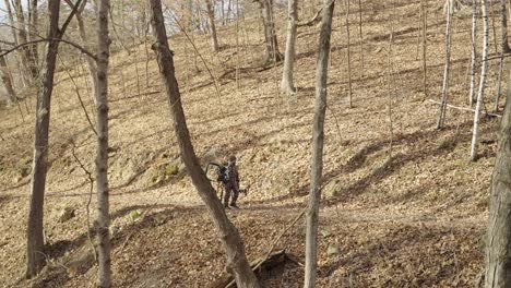 Bowhunter-man-carrying-hunting-equipment-walking-outdoors-in-winter-forest-path