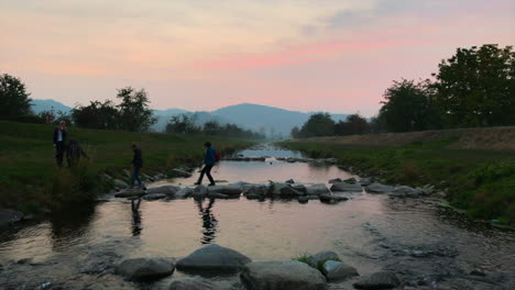 Menschen,-Die-Einen-Fluss-Mit-Dem-Orangefarbenen-Himmel-Im-Hintergrund-überqueren,-Lautenbach,-Deutschland