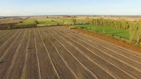 Amplia-Vista-De-Las-Hermosas-Tierras-De-Cultivo-Planas-De-Canadá-Mientras-Un-Tractor-Trabaja-En-Un-Campo-Marrón-Polvoriento