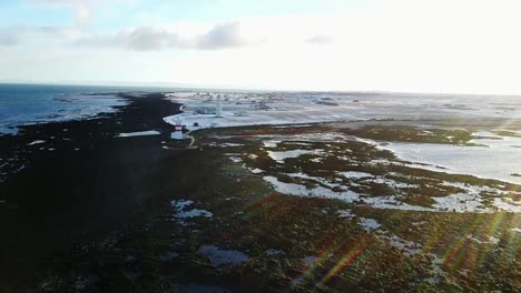 Aerial-shot-pulling-away-from-tip-of-Sangerdi,-Iceland-during-sunset-with-flares-beaming-across-frame