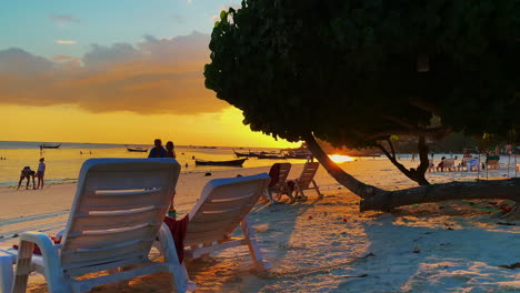 Ein-Shott-Am-Strand-Mit-Menschen,-Die-Mit-Orangefarbenen-Sonnenuntergängen-Spazieren-Und-Plaudern