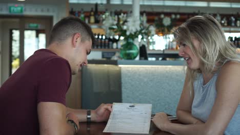 Joven-Pareja-Atractiva-En-Una-Cita-Interactuando-Y-Mirando-El-Menú-En-Un-Restaurante-De-Lujo