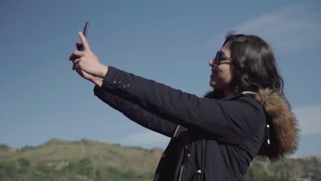 Narrow-shot-of-a-girl-taking-selfie-and-pictures-with-blue-sky-and-landscape-in-slow-motion