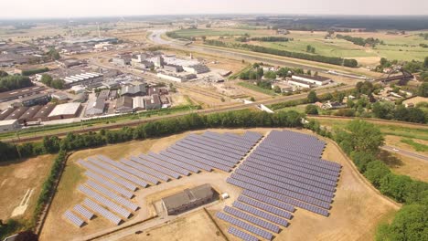 Una-Toma-Aérea-Suave-De-ángulo-Alto-Que-Revela-Una-Granja-Solar-Debajo-Con-Industria-Y-Vías-Fluviales-Activas-Que-Transportan-Mercancías