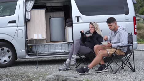 Joven-Pareja-Atractiva-Sentada-Y-Almorzando-Con-Autocaravana-Junto-Al-Lago-Wakatipu,-Queenstown,-Nueva-Zelanda