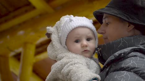 Junge-Mutter,-Die-An-Einem-Kalten-Wintertag-Im-Freien-Einen-Kleinen-Jungen-In-Einer-Süßen-Weißen-Kleidung-Hält