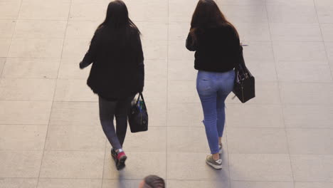 Two-young-women-walking-towards-a-train-platfrom,-slow-motion-footage-of-Antwerp-Central-Station-during-a-sunny-day