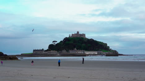 Niños-Jugando-Con-Una-Cometa-En-La-Playa-De-Marazion-En-Cornualles-Con-El-Castillo-Medieval-Inglés-Y-La-Iglesia-Del-Monte-De-San-Miguel-Detrás