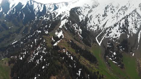 Aerial-drone-snow-capped-mountains-landscape-with-green-forest-during-cloudy-rainy-weather