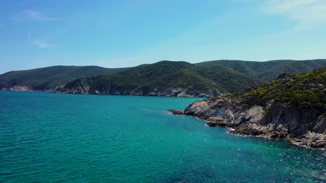 Hidden-beach-discovered-behind-rocky-coastline-and-crystal-clear-blue-sea-in-the-Mediterranean-aerial-footage