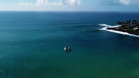 Drone-Shot-following-a-sailboat-standing-still-in-Waimea-Bay,-on-the-North-Shore-of-Oahu,-Hawaii