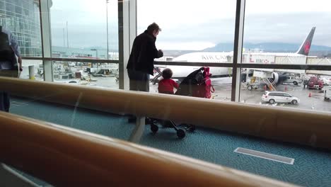 Un-Hombre-Y-Un-Niño-Miran-Por-La-Ventana-En-Un-Aeropuerto-Y-Ven-Un-Avión-De-Air-Canada