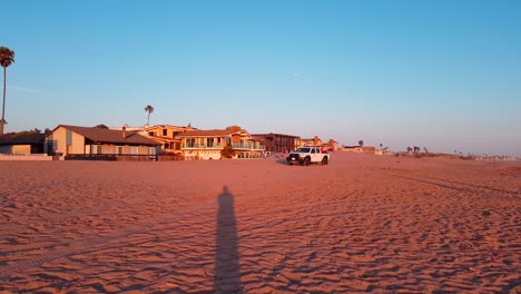 Shot-following-Lifeguard-pickup-truck-driving-on-beach-of-San-Buenaventura-State-Beach-at-sunset-in-Ventura,-California,-United-States