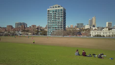 A-couple-is-watching-office-workers-playing-soccer-during-a-lunch-break-on-a-sunny-day