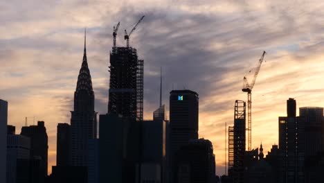 Establishing-shot-of-Chrysler-building,-the-Metlife-building-and-the-construction-of-new-skyscrapers-at-sunset,-while-a-helicopter-flying-by-in-the-background-in-New-York-City