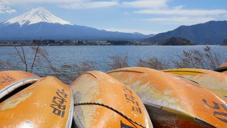 Vista-De-La-Montaña-Volcánica-Fuji-Con-El-Lago-Kawaguchi-Y-Un-Grupo-Naranja-De-Pequeños-Botes-En-Canoa-Cerca-De-La-Orilla-En-El-Día-De-Cielo-Despejado-De-Primavera