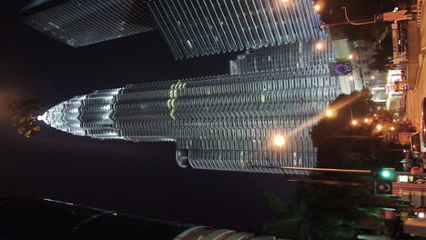 Video-Vertical-De-Las-Torres-Gemelas-Petronas-De-Singapur-En-La-Noche-Con-Farolas,-Street-View