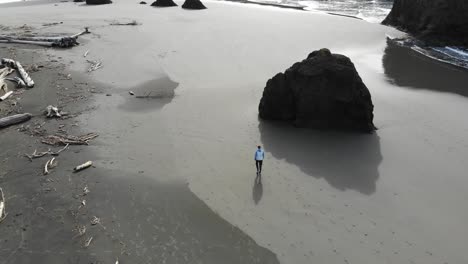 Die-Drohne-Folgt-Einem-Mann-Am-Strand,-Der-In-Richtung-Seestapel-Geht