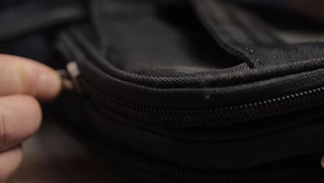 Hand-pulling-metal-zip--to-open-black-briefcase
