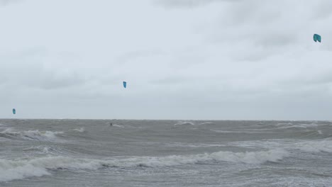 Kite-surfing-surfers-sailing-on-the-big-Baltic-sea-waves-at-Liepaja-Karosta-beach,-overcast-autumn-day,-wide-shot