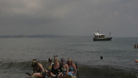 Local-business-Cornwall-team-dressed-as-'DC'-comics-superheroes-finishing-at-the-Newlyn-raft-race-charity-fun-outdoors-event,-Panning-shot