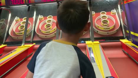 Kamera,-Die-Sich-Auf-Einen-Kleinen-Jungen-Konzentriert,-Der-Skee-Ball-In-Einer-Spielhalle-Spielt