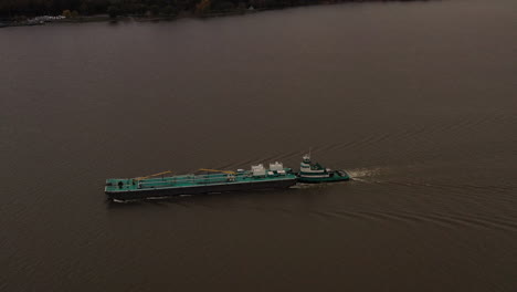 aerial-shot-over-a-turqiuse-colored-barge---tugboat-on-the-Hudson-River-on-a-cloudy-day-in-Beacon,-NY
