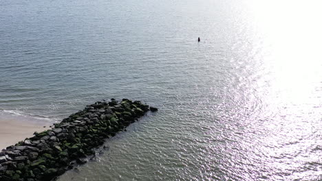A-bird's-eye-drone-view-of-a-stone-jetty-as-the-ocean-waves-gently-crash-onto-the-shore