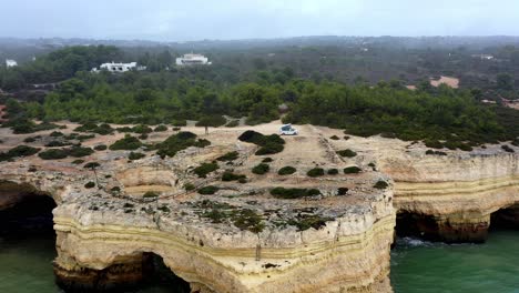 Sea-carved-caves-at-the-beach-in-the-south-of-the-country-with-camping-van-parked-on-top,-Aerial-dolly-out-reveal-shot