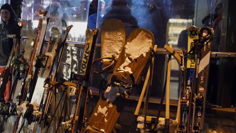 Toma-Fija-Centrada-En-Diferentes-Tablas-De-Snowboard-Y-Esquís-Que-Se-Muestran-Fuera-De-Una-Discoteca,-Gente-Bailando-Dentro