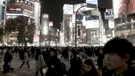 Shibuya-crossing-with-thousands-of-people-walking-at-night-overlooking-illuminated-signs,-handheld-shot