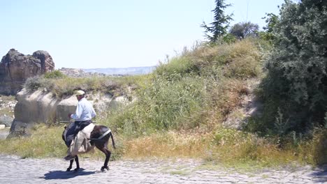 Mann-In-Kappadokien,-Türkei,-Reitet-Esel-Auf-Einer-Staubigen-Straße-In-Der-Nähe-Der-Wüste