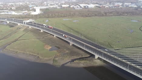 Aerial-tracking-view-above-vehicles-commuting-on-bridge-motorway-over-river-Mersey,-UK