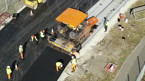 Aerial-view-of-workmen-spreading-newly-laid-tarmac-on-a-road
