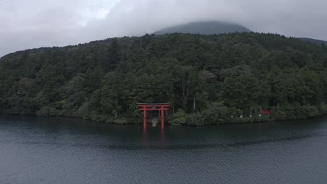 Drone-pull-back-reveal-shot-of-Lake-Ashinoko-with-a-red-Torii-gate-in-Fuji-Hakone-Izu-National-Park,-Japan