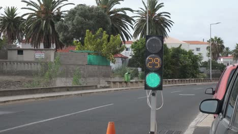 Temporary-portable-traffic-light-with-timer-and-colors-from-red,-amber-to-green-by-asphalt-road-with-cars-driving-and-passing-by-in-tropical-Porto-Santo-downtown-city-center,-Portugal,-static-close-up