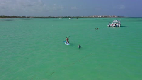 People-swim-and-paddle-board-around-Luxury-yachts-anchored-in-exotic-Tropical-Dominican-republic-ocean-water,-Drone-Aerial